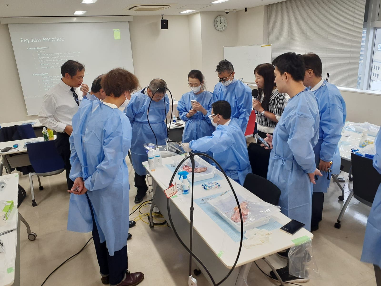 Clinical demonstration with dental professionals in protective gowns observing a hands-on practice exercise