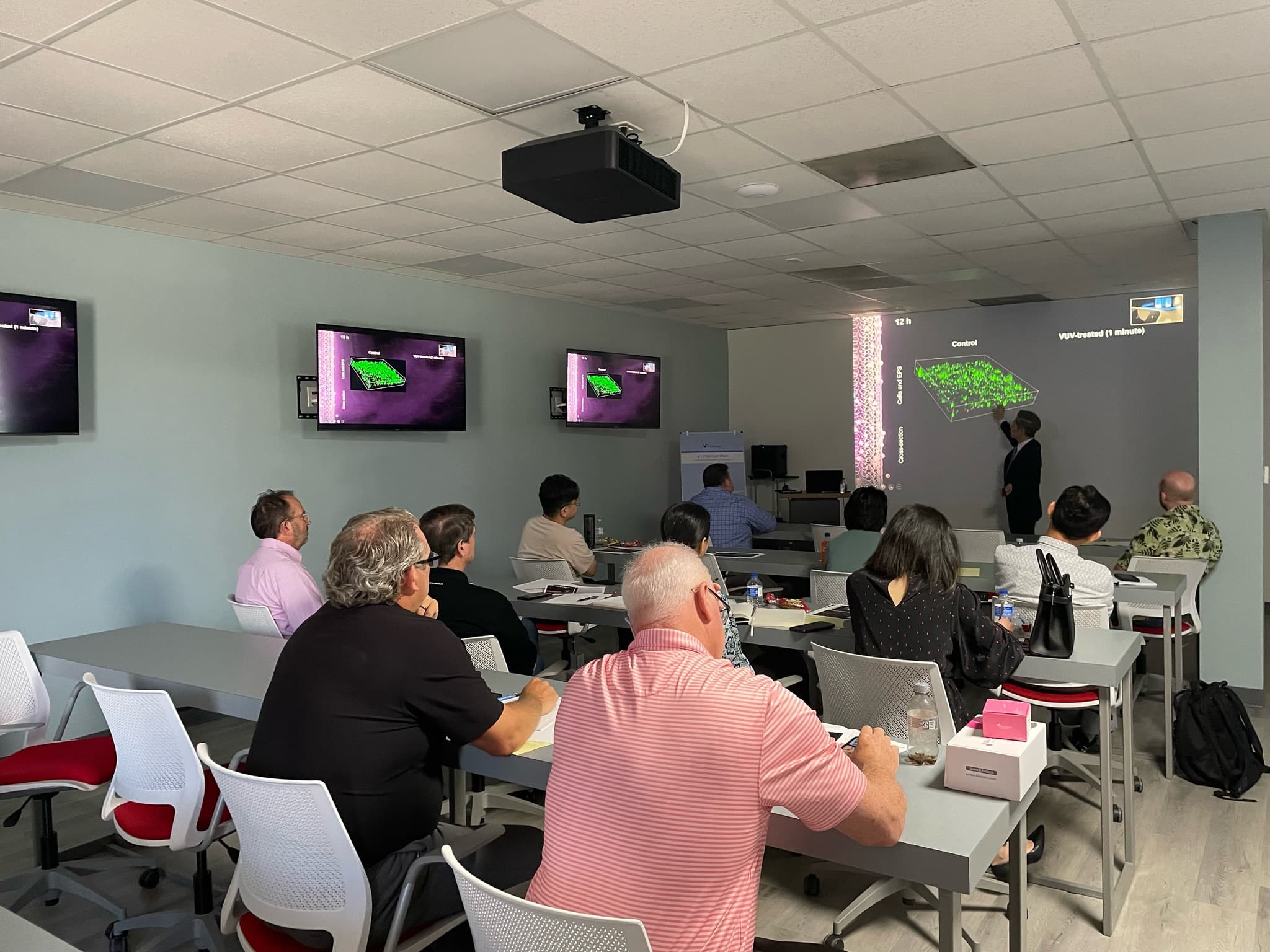 Lecture room with seminar seating, wall displays, and a live presentation